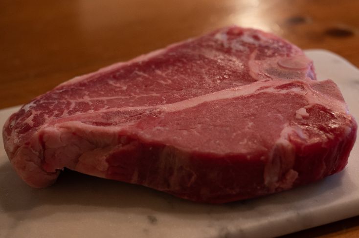 Prime rib cooked beautifully on a white plate, resting on a wooden dining table.